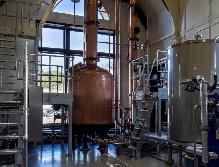 A large copper vat and distilling equipment in a building with large windows.