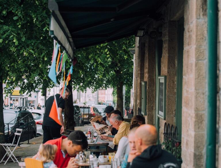 People eating and drinking on outside tables at an eatery in a book town.