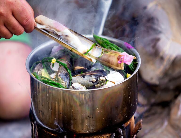 A pot of mussels cooking on an open fire.
