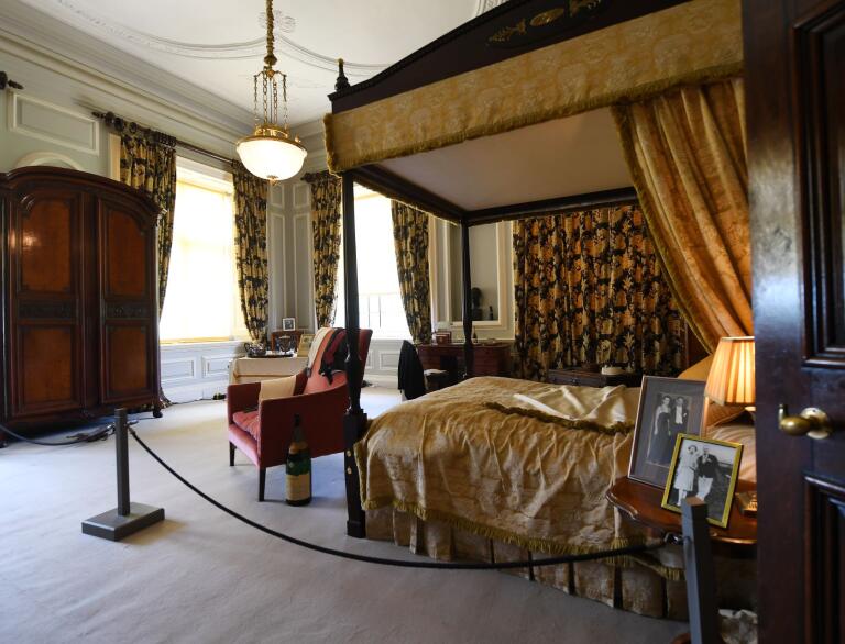 A four poster bed, armchair and wardrobe in a grand room of a stately home.