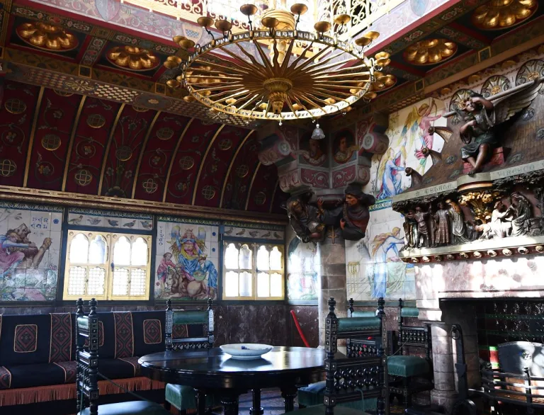 An ornate grand room with a chandelier hanging above a dining table next to a fireplace.