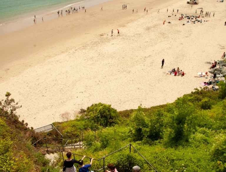 People walking down steps to a beach with a pastel coloured town in the background.