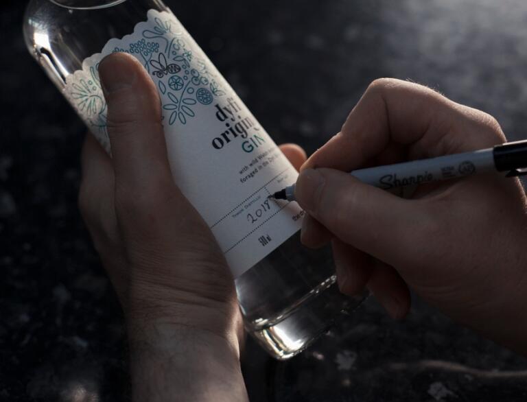 A man writing the distilled date on a bottle of gin.