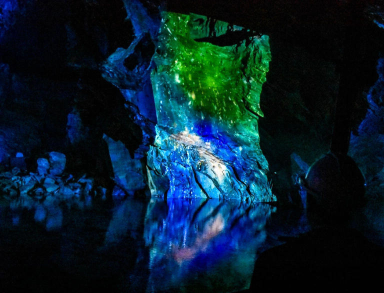Slate rocks in an underground cavern lit up in colour, reflecting in the water.