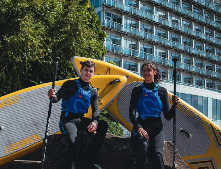 Two paddleboarders standing outside a hotel.
