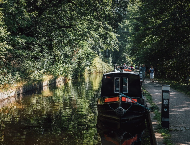 Narrowboats moored on the side of a canal with people walking the towpath.