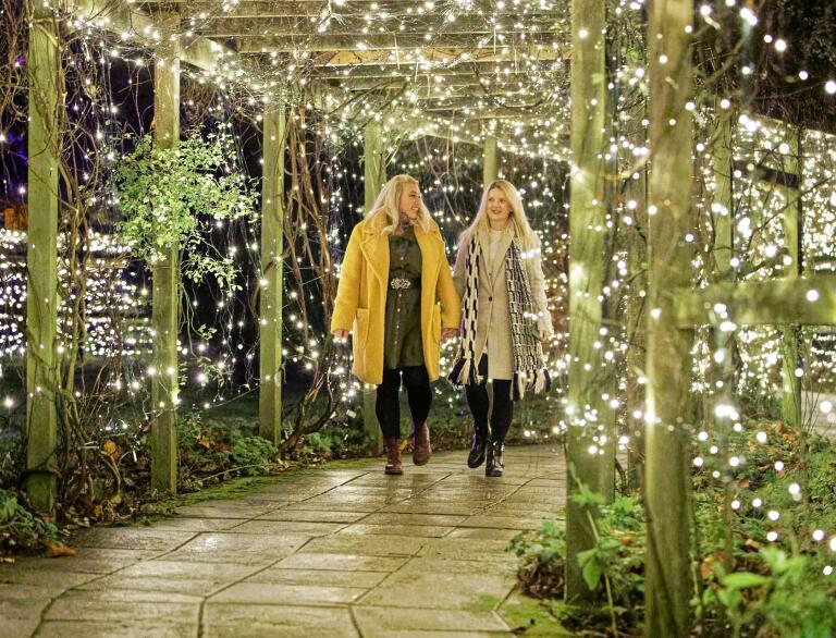 Ladies walking through a timber covered path lit with fairy lights.