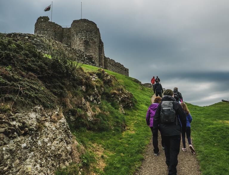 People walking up a hill toward the entrance of a castle.