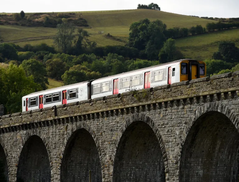 A train travelling along a viaduct, with green hills in the background.