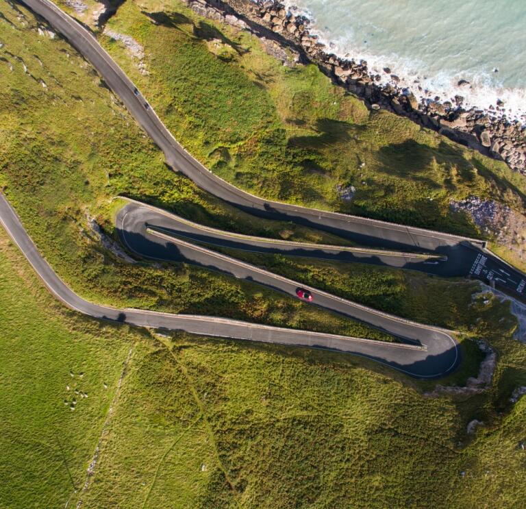A car driving a zig zag road on a headland by the coast.