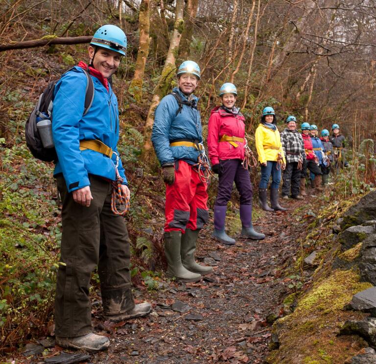 People lined up on a path smiling at the camera in caving gear.