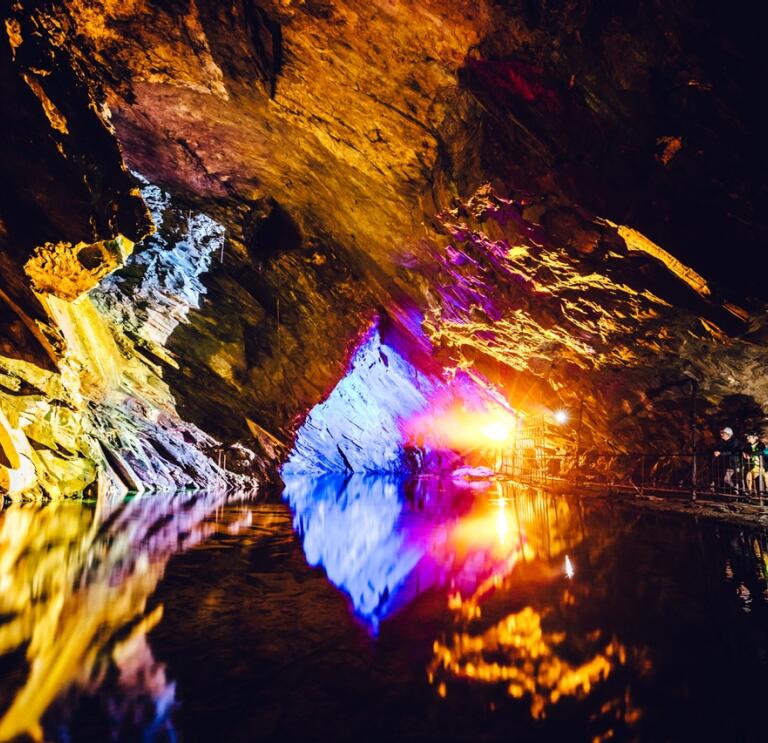 Underground slate cavern colourfully lit and reflecting in the water.