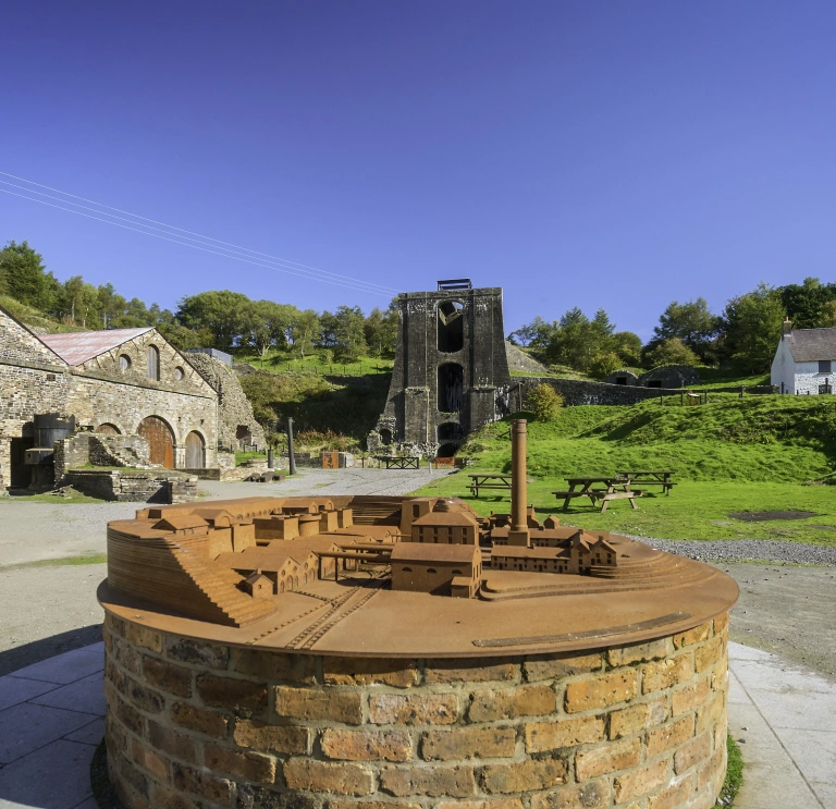 A small scale model of the ironworks at Blaenavon, with real site behind it.