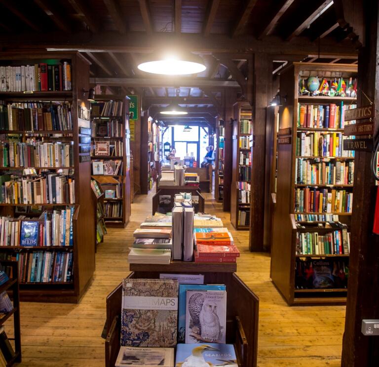 The aisle of a book shop with shelves either side full of books in Hay on Wye.