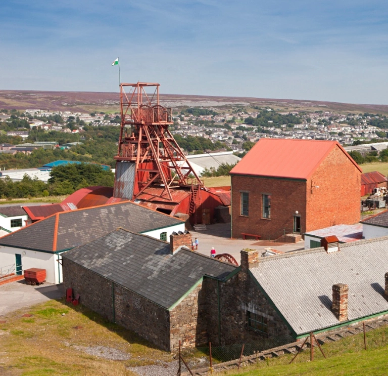 Colliery buildings and a pit head overlooking a town in the South Wales valleys.