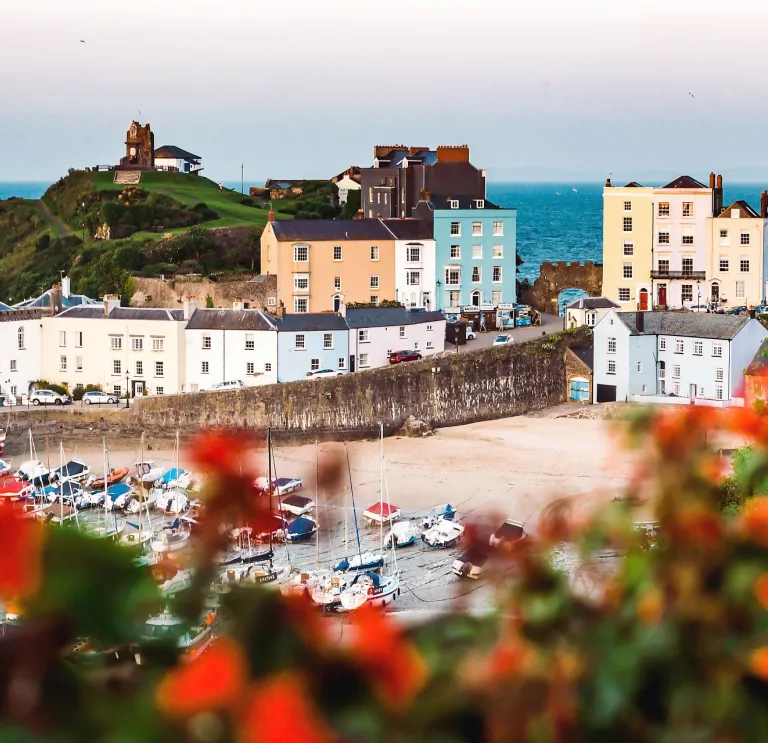 Looking down toward a harbour with boats on the sand and colourful houses and the sea in the background.