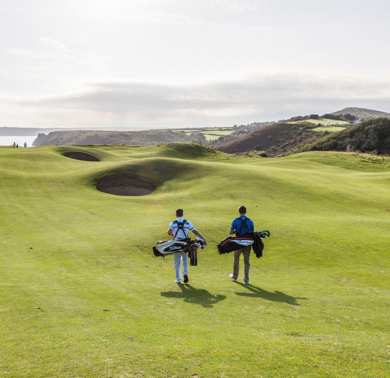 Golfers walking to the next tee with views of the coastline.