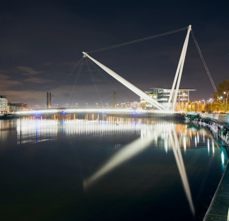 Night time view of the river with reflective white lights from the bridge and buildings on the right of the image