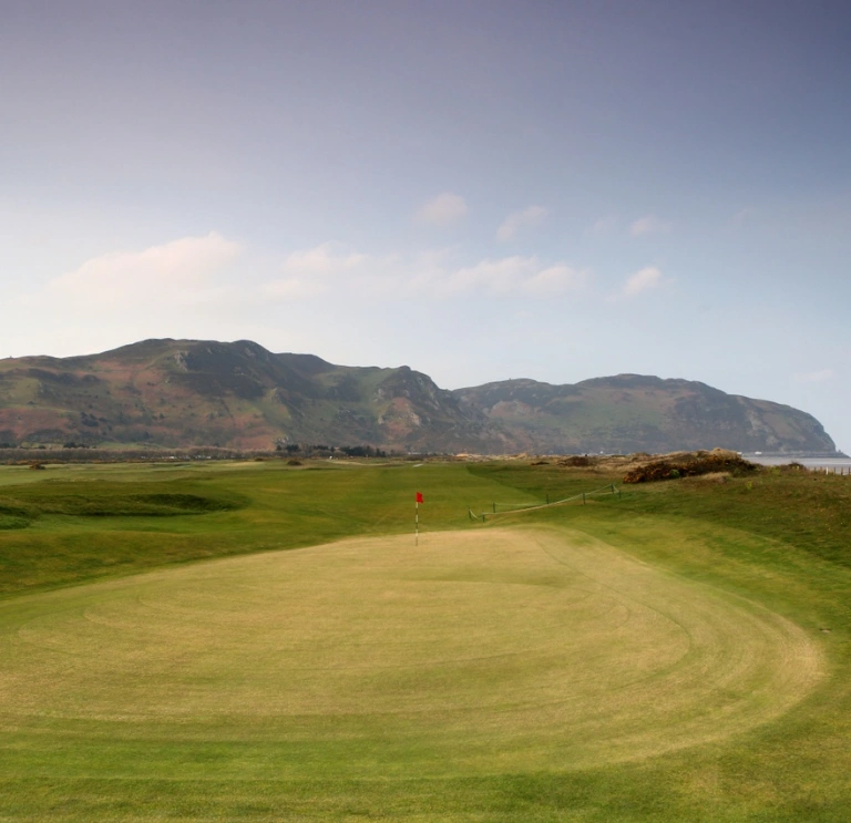 The green on a golf course with views of the coastline and cliffs beyond.