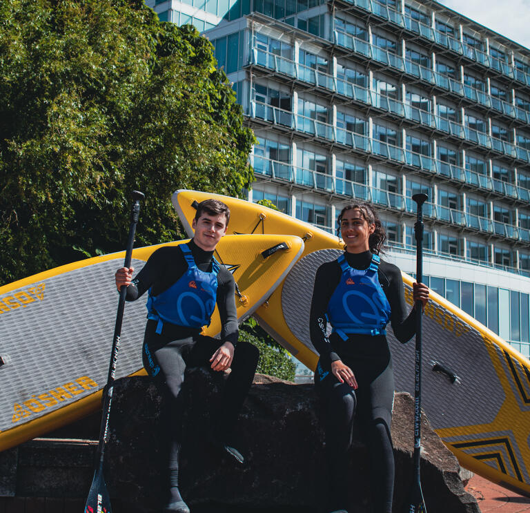 Two paddleboarders standing outside a hotel.