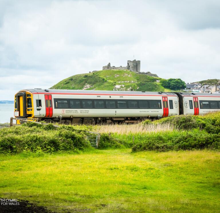 A train travelling alongside the coast and a castle on a hill.