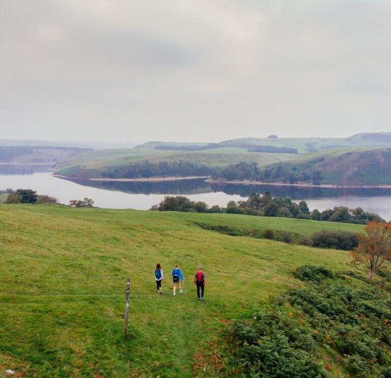 Walkers on a hill overlooking a reservoir.
