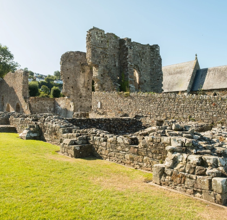 The ruins of an abbey with a church in the background.