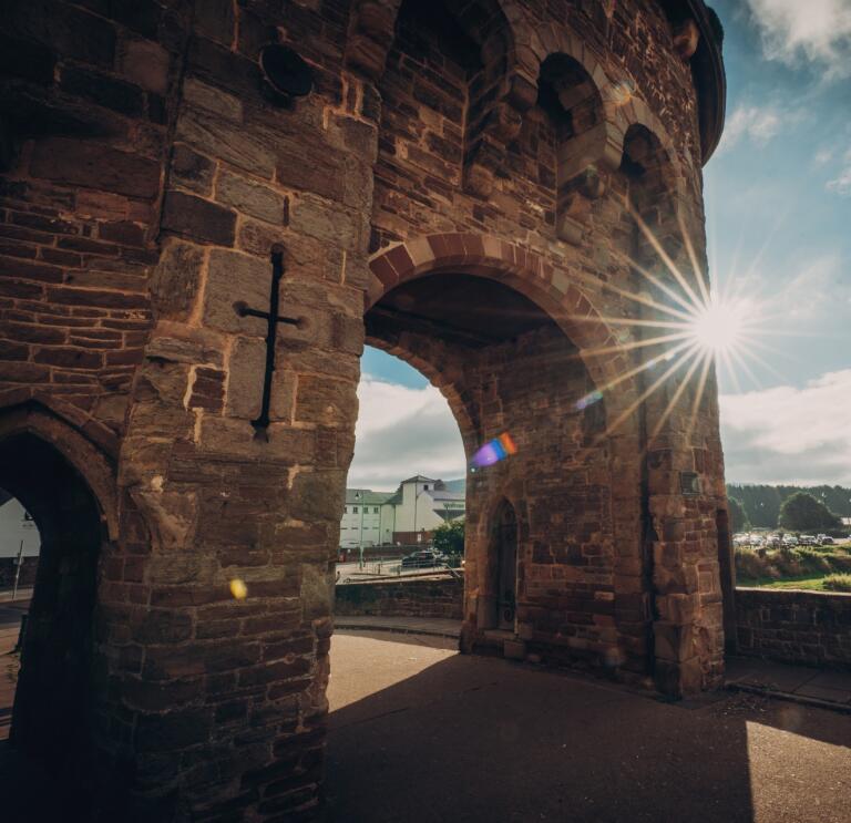 The sun shining against a medieval fortified river bridge.