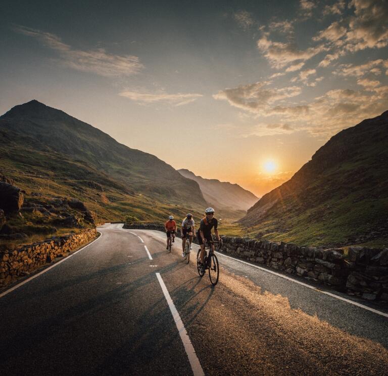 Group of cyclists on a mountain road with the sunsetting beyond.