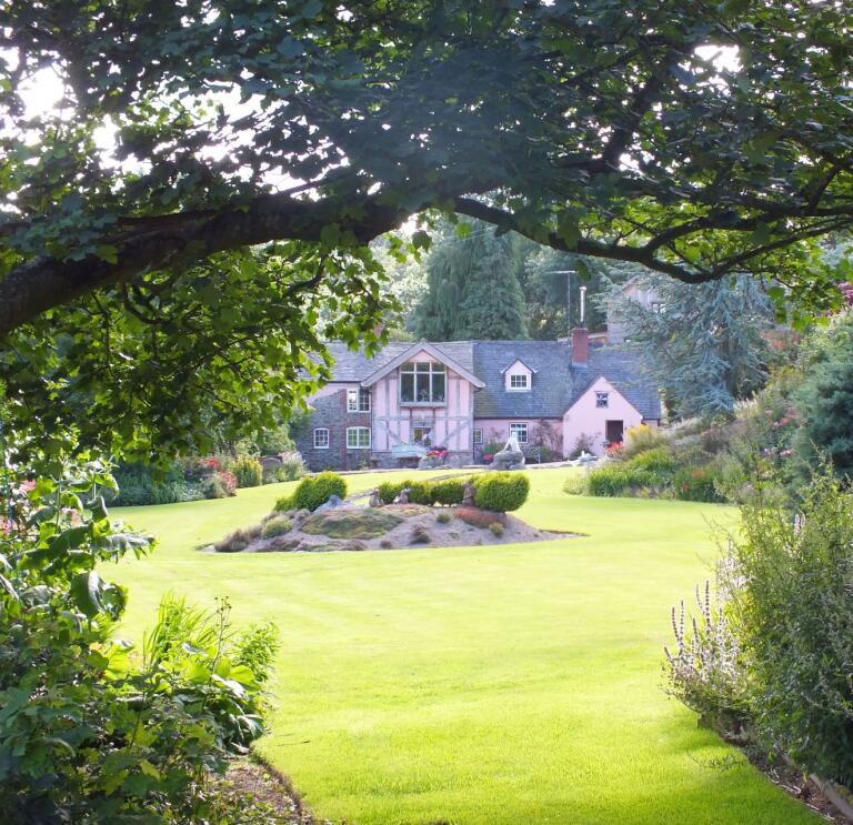 A house amongst a beautiful lawn and gardens.