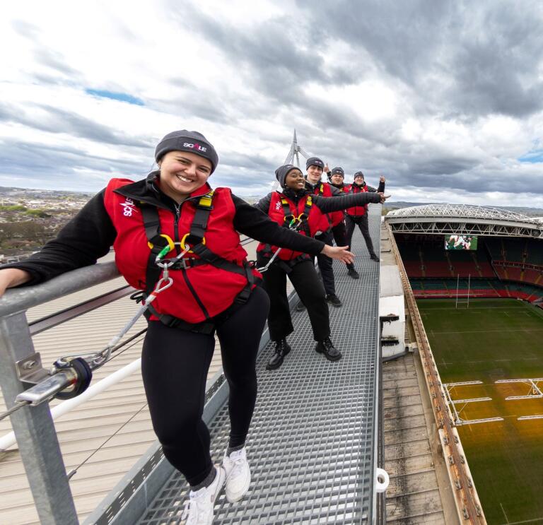 Group of people in safety gear on a roof at a sports stadium.