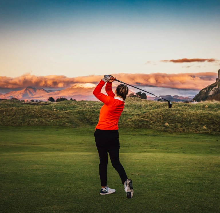 A golfer taking a shot with a castle in the foreground.