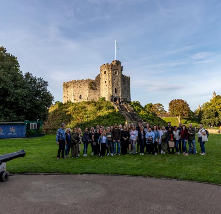 Group of people standing at the foot of a castle smiling at the camera.