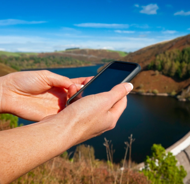 Female walker using iPhone near a reservoir.