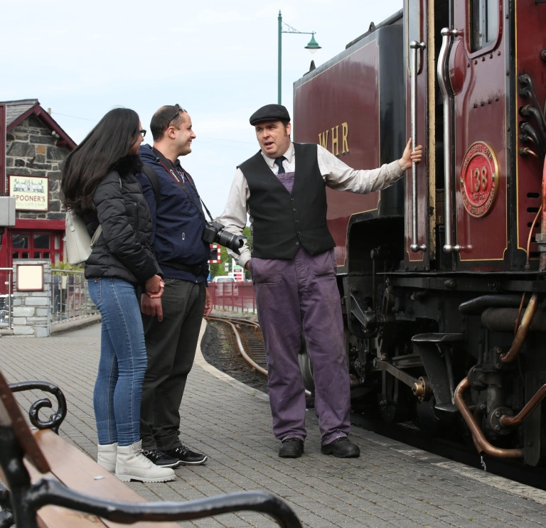 A couple talking to the driver next to a steam train.