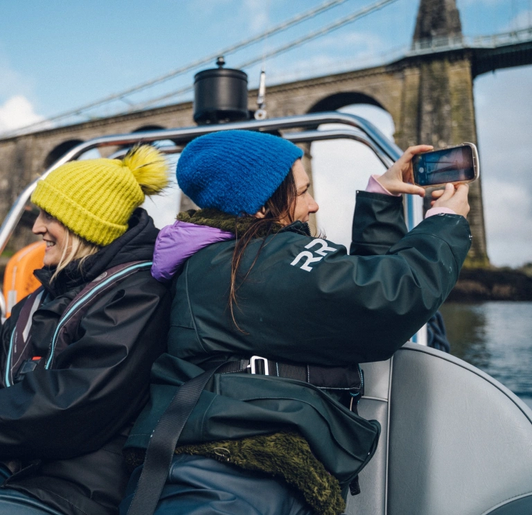 Group of ladies on a speed boat with one taking a photo of a bridge.