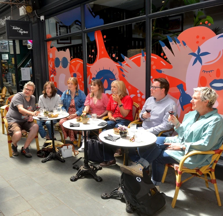 Group of people sitting a a table eating and drinking on a food tour in a shopping arcade.