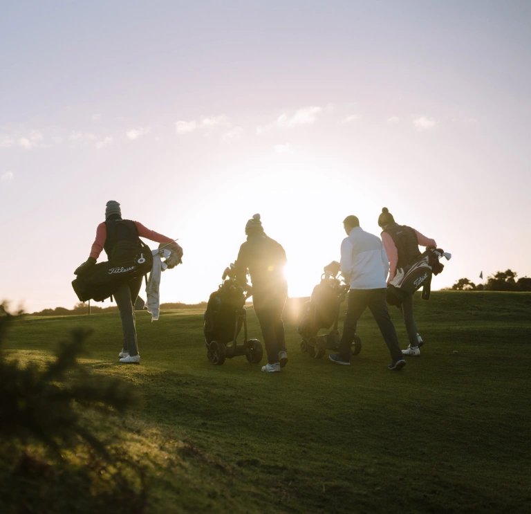 Golfers walking to the next tee on a golf course at sunrise.