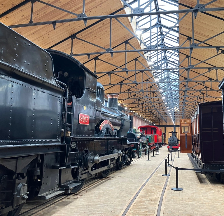 An engine shed filled with steam trains and carriages.