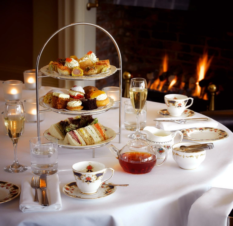 A table set up for afternoon tea with champagne next to a roaring fire.