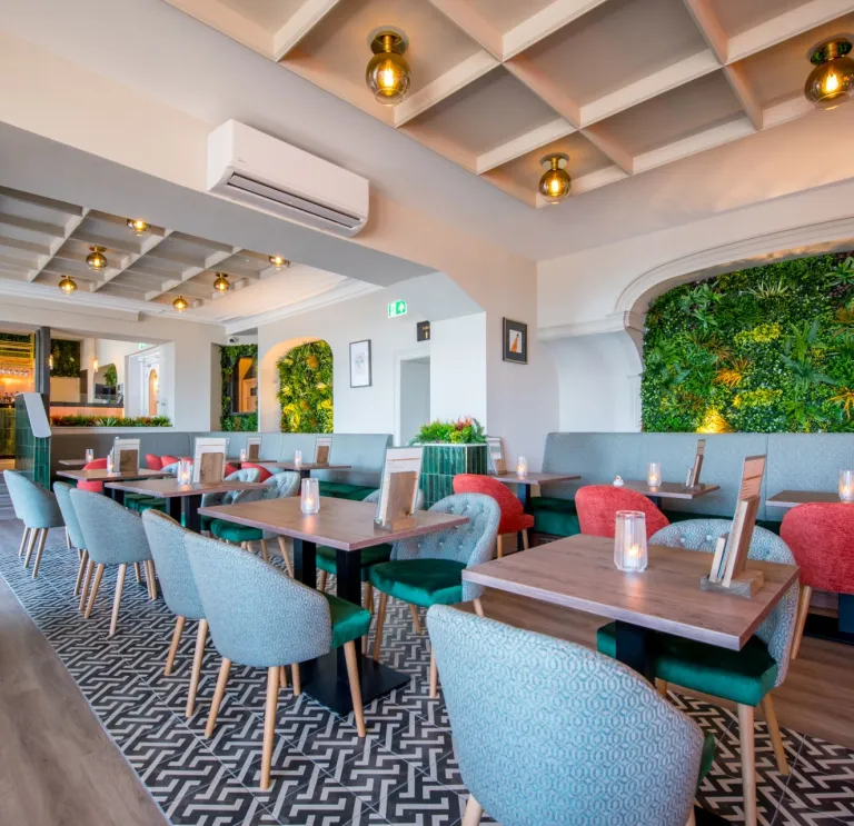 Hotel restaurant with small tables and chairs and greenery