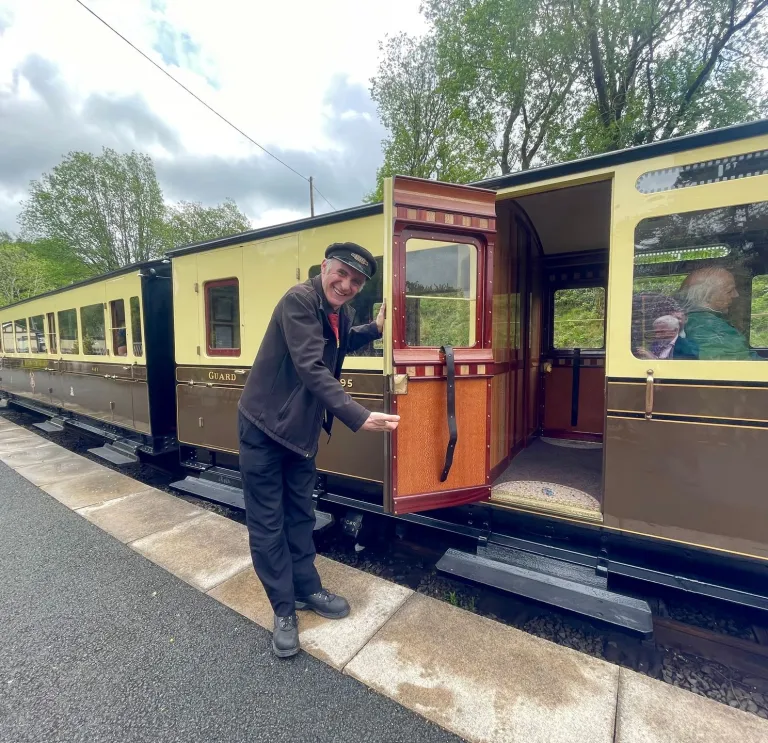 Man holding open a door of train carriage on a steam train.