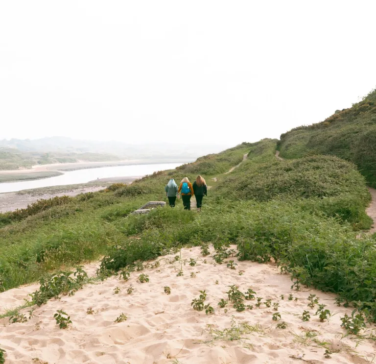 Group of ladies walking along sand dunes toward the beach.