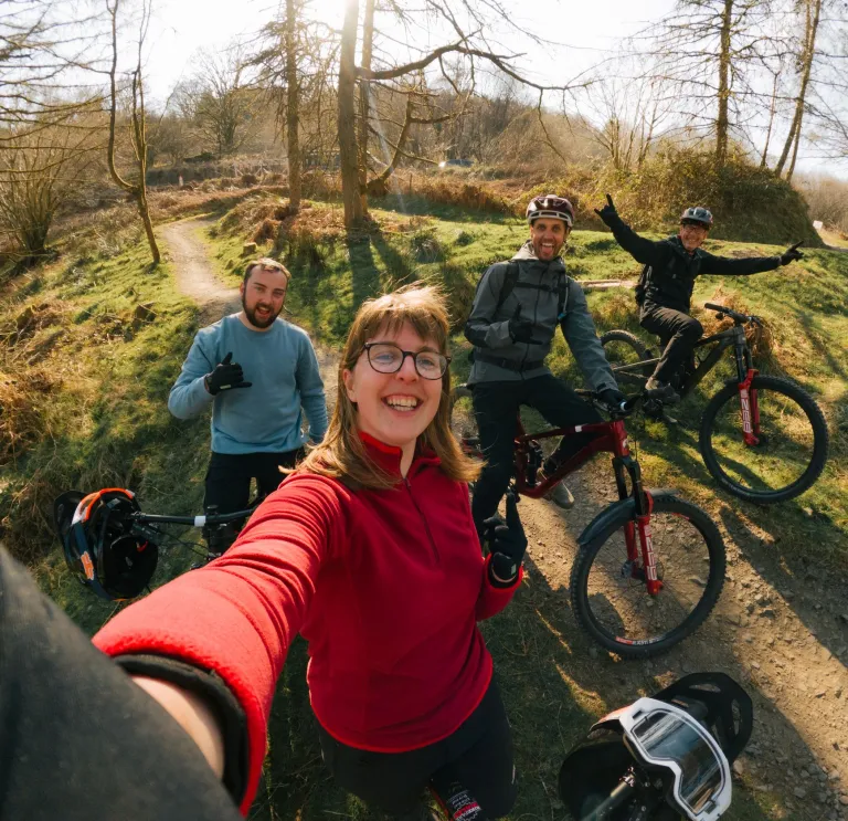 Group of people with their bikes in a bike park smiling at the camera.