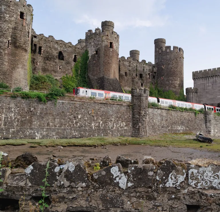 A train coming out of a turret on a castle wall with the castle beyond.
