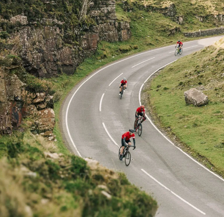 Cyclists on a road against a mountainous landscape with a Welsh dragon on the wall.