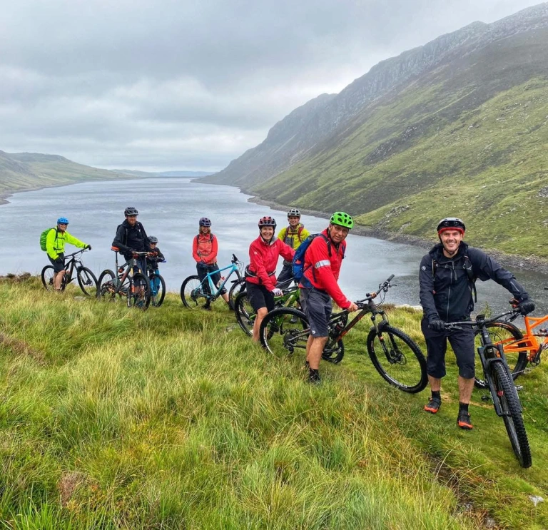 Group of cyclists surrounded by a lake and mountains.