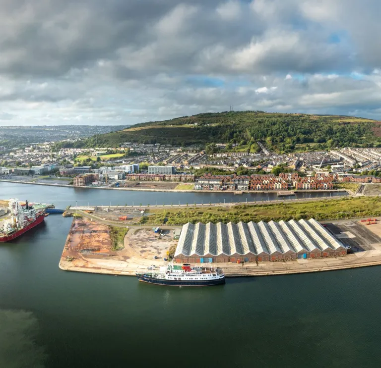 Aerial shot of a cruise shop docked at a port, witgh green mountains beyond.