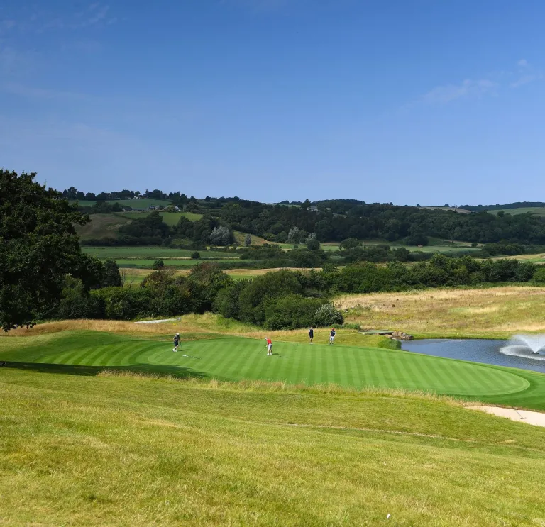 Golfers putting on the green of a golf course next to a fountain.