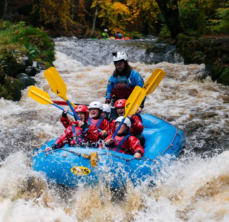 Group of people on a raft heading down rapids on a river.
